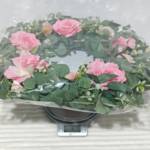 Close-up of pink camellia and eucalyptus wreath being weighed on a scale for shipping
