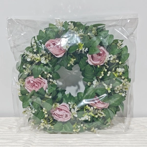 Detailansicht eines rosa künstlichen Rosenkranzes mit grünen Blättern in einer Polybeutel