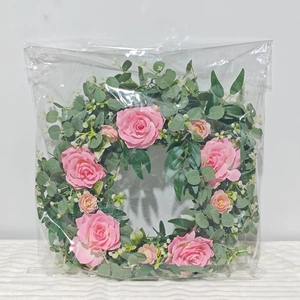 Detailed view of artificial pink camellia and eucalyptus wreath in protective clear packaging