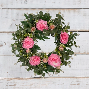 Pink camellia and eucalyptus wreath for front door on white wooden background
