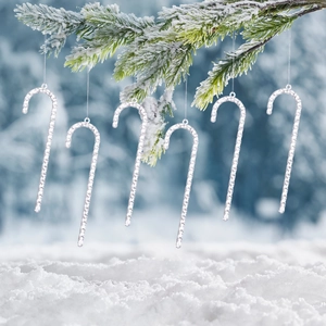 Set of 6 transparent acrylic icicle candy cane ornaments hanging on a snowy pine branch