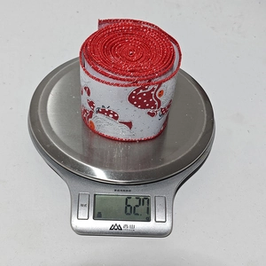Detailed view of 62.7g Christmas ribbon roll with mushroom and ladybug patterns on a scale