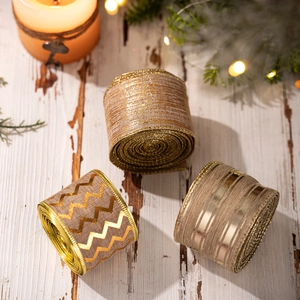 Three rolls of gold Christmas burlap ribbon set on a rustic wooden background with candles
