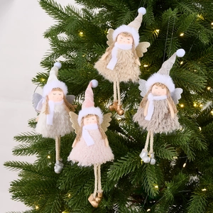 Pink and beige plush Christmas angel ornaments with wings hanging on a lit Xmas tree