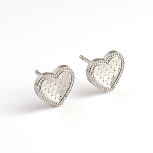 Dettaglio degli orecchini a cuore in argento con trama a scaglie lucide e bordo perlato