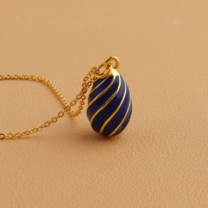 Detailed close-up of blue enamel egg pendant with gold spiral texture and fine chain