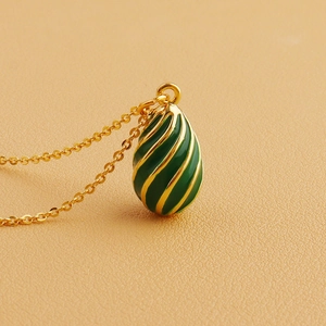 Detail of vintage 18k gold plated green enamel egg pendant with spiral texture