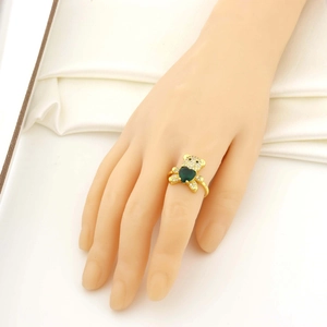Détail d'une bague ours dorée avec une pierre en forme de cœur vert portée à la main