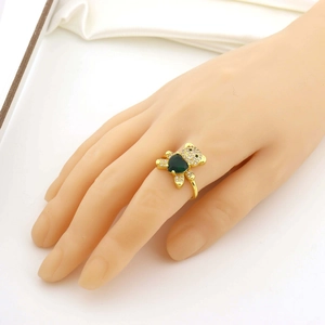 Détail d'une bague ours avec pierre cœur verte et zircons sur main avec tissu en soie