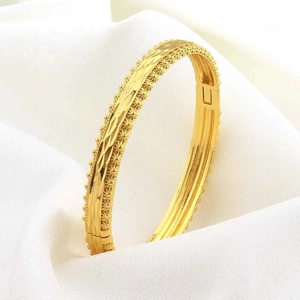 Dettaglio di un bracciale dorato con trama a diamante e bordo perlato su seta