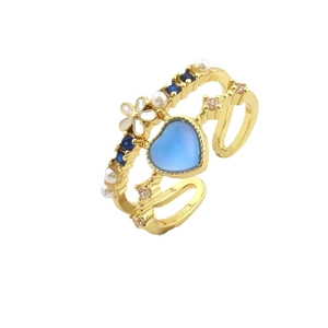 Bague réglable dorée avec pierre cœur bleue, fleur blanche et perles sur fond blanc brillant