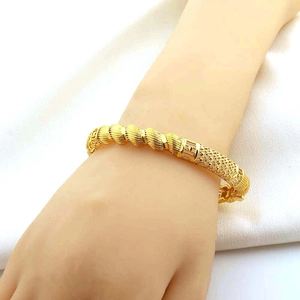 Detailopname van een 18K vergulde gedraaide armband om de pols tegen witte stoffen achtergrond