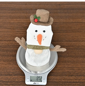 Detailed view of handmade Christmas plush snowman on scale weighing 87.2g on wood table