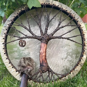 Handcrafted shamanic tree of life frame drum with fur-wrapped mallet on green grass