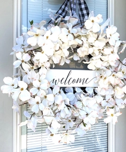 Detail of white dogwood wreath with a welcome wooden sign and buffalo plaid ribbon