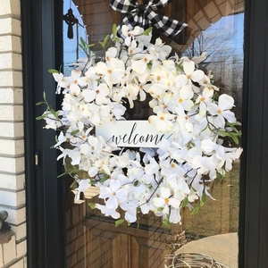 Detail of a welcome wreath with white dogwood flowers and a black-white buffalo plaid bow