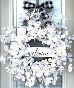 Detail of white dogwood wreath with a welcome wood sign and buffalo check bow