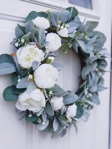 Detailed view of artificial white peony wreath with flocked greenery on a white wooden door