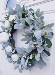 Close-up of artificial floral wreath with lamb's ear leaves and white roses on a white door