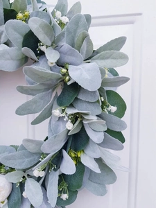 Close-up of artificial lambs ear and eucalyptus wreath with white flowers on a white door