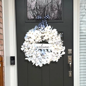 Close-up of artificial dogwood wreath with buffalo plaid bow and welcome sign on door