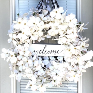 Detail of white dogwood wreath with a welcome sign and black and white buffalo plaid ribbon