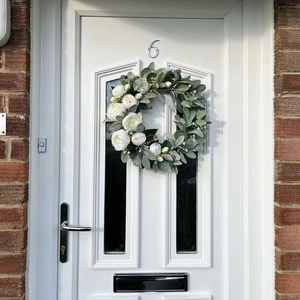 Realistic white peony wreath with greenery hanging on a white front door as decoration