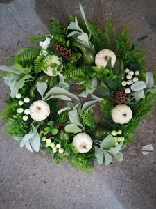 Close-up of white mini pumpkins, pine cones, and green leaves on an autumn harvest wreath