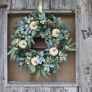 Fall wreath with white pumpkins, eucalyptus leaves and pine cones on a rustic door