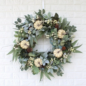 Autumn wreath with white pumpkins, pine cones and eucalyptus leaves on a white brick wall