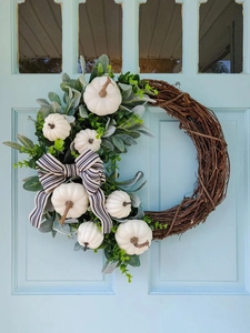 Detailweergave van herfstkrans met witte pompoenen, saliebladeren en een gestreepte strik