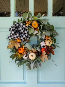 Detail von Herbstkranz mit Kürbissen, Tannenzapfen und Karoschleife an blauer Tür
