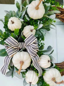 Detail van een herfstkrans met witte pompoenen, salieblaadjes en een gestreepte strik erop