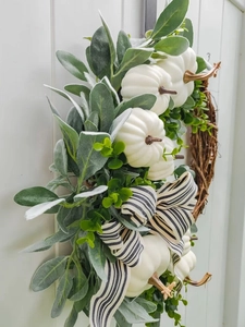 Detail van witte pompoenen en lamsoorbladeren op een herfstkrans met gestreepte strik