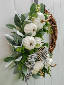 Detail van witte pompoenen en groene bladeren op een krans met een gestreepte strik