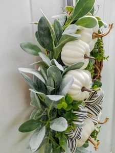 Detail van witte pompoenen en gestreepte strik op herfstkrans met groene bladeren