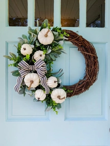 Detail van herfstkrans met witte pompoenen en blauw gestreepte strik op houten deur