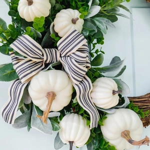 Herfstkrans met witte pompoenen, groene bladeren en zwart-wit gestreept lint decoratie