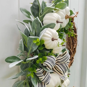 Herfstkrans met witte pompoenen, ezelsoorbladeren en zwart-wit lint op houtdecor