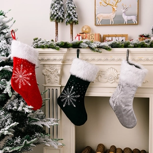 Three premium velvet Christmas stockings with snowflakes hanging on a white fireplace