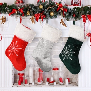 Three premium velvet Christmas stockings with snowflakes hanging on a festive white fireplace