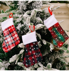 Close-up of three plaid Christmas stockings with snowflake patterns on festive tree branch