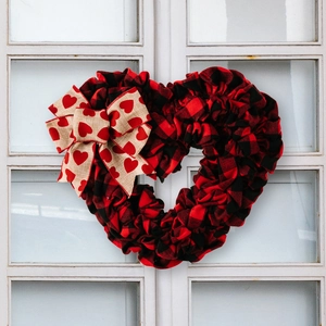Close-up of red and black buffalo plaid heart wreath with a burlap bow on a glass window