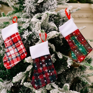 Three plaid Christmas stockings with white snowflake patterns hanging on a snowy tree