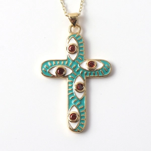 Detail of gold-plated cross necklace with blue enamel evil eye and red zircon center