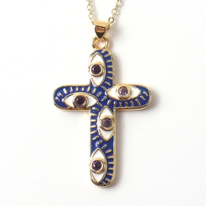 Close-up of gold cross pendant with blue enamel evil eye motifs and purple gems