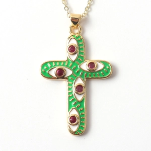 Detail of gold cross pendant with green enamel eye pattern and red zircon stones