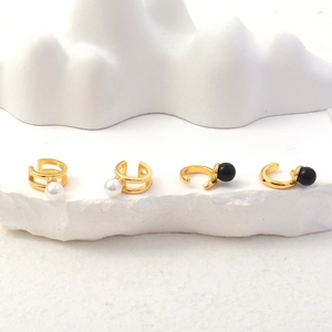 Nahaufnahme goldener Ohrclips mit schwarzen und weißen Perlen auf minimalistischem Stein