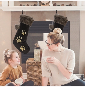 Détail de chaussettes de Noël en velours avec empreintes de pattes dorées près du foyer