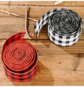 Close-up of red and black buffalo plaid ribbons on a rustic wood background with pine cones